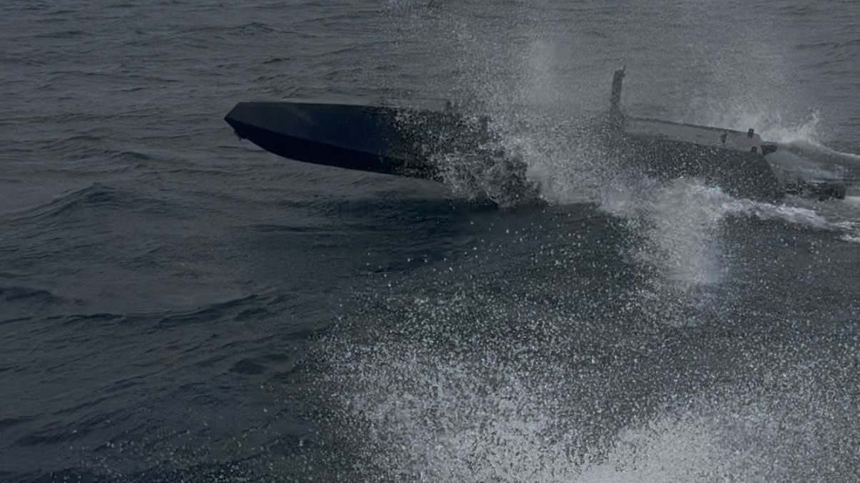The six metre uncrewed hull under way in a short sea, bow lifted, throwing spray down its port side.